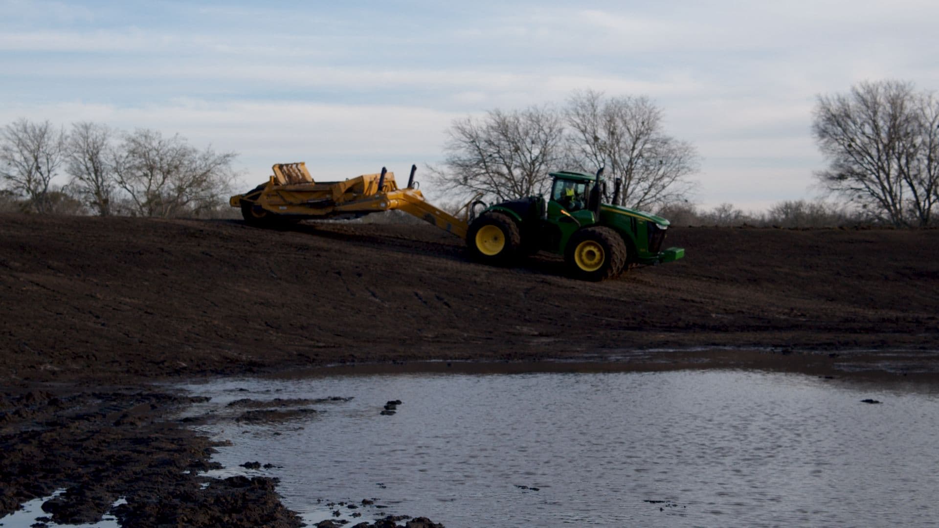 A tractor shaping an earthen dam beside a filling Texas lake